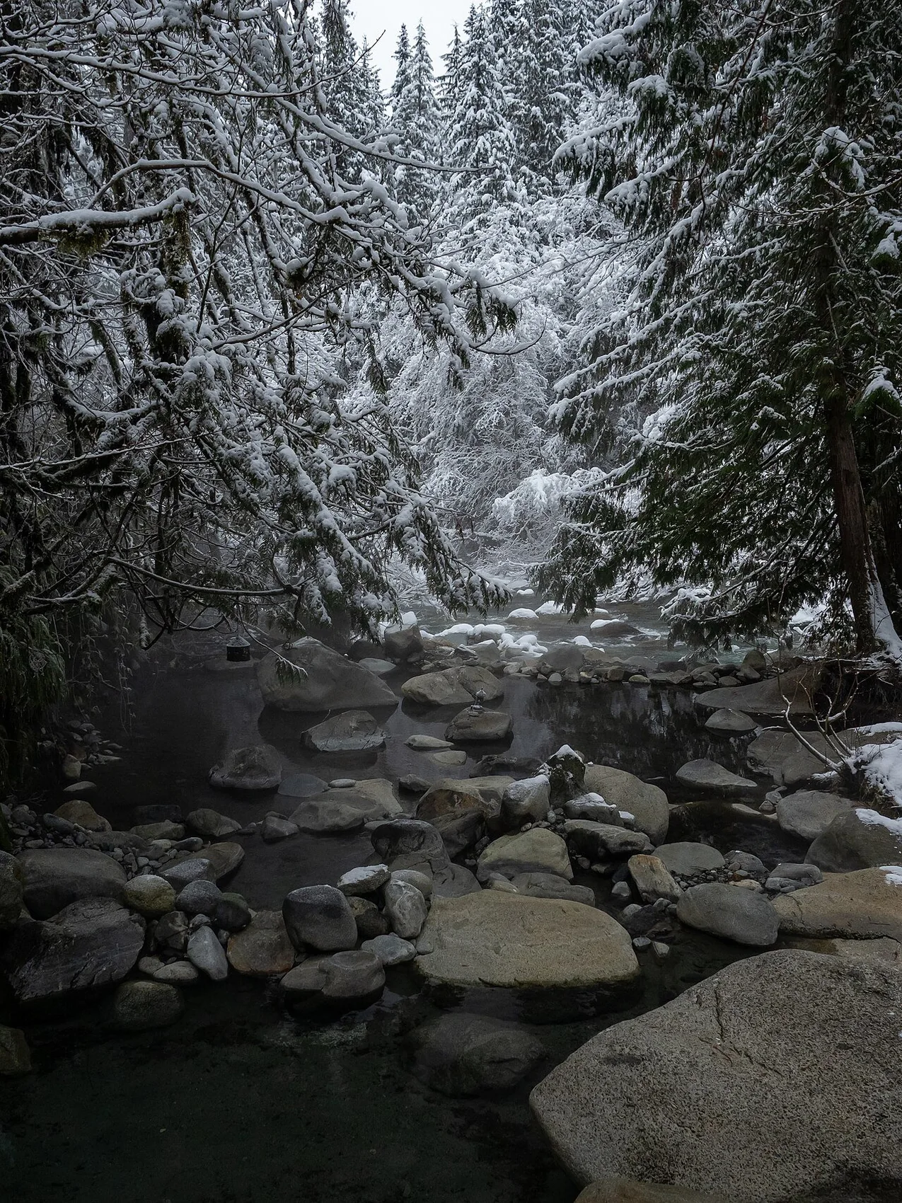 Rock-lined thermal pools in snowy forest at Sloquet Hot Springs (archive photograph)